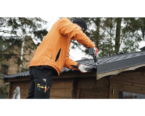 Handwerker montiert mit einem Akkuschrauber Dachpappe auf einem Gartenhaus.