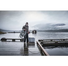 Mann mit Seil auf einem Holzsteg am Wasser mit einer Kühlbox