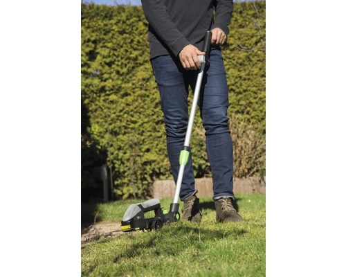 Eine Person verwendet einen Rasenkantenschneider zur Rasenpflege im Garten.