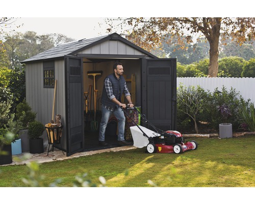 Ein Mann schiebt einen Rasenmäher aus einem Gartenschuppen in einem Garten.