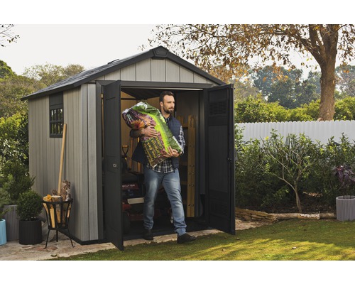 Mann trägt Pflanzerde aus einem grauen Gartenhaus mit geöffneten Türen