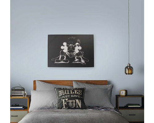 Schlafzimmer mit Bett, Nachttischen, Lampe und Wandbild mit Mickey Maus Motiv