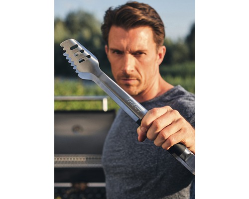 Mann hält Grillzange aus Edelstahl in die Kamera