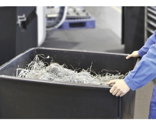 Eine Person hält eine schwarze Wanne gefüllt mit Metallspänen.