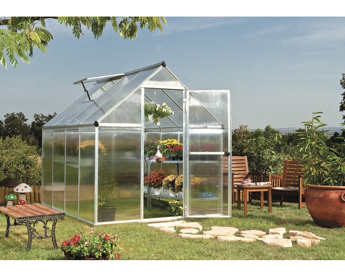 Gewächshaus mit geöffneten Türen und Regalen voller Blumen in einem Garten.