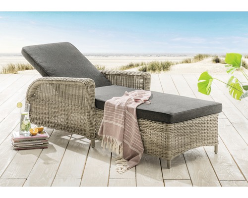 Geflochtene Gartenliege mit grauer Auflage vor Strandkulisse