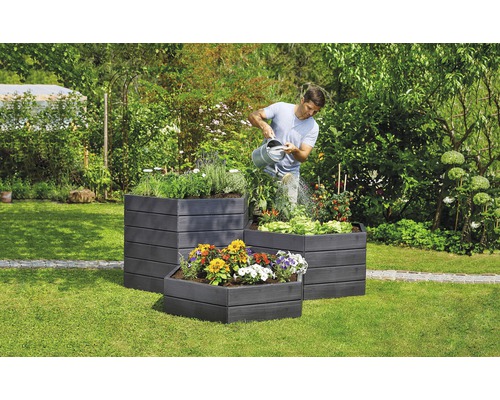 Mann gießt Pflanzen in drei Hochbeeten im Garten.