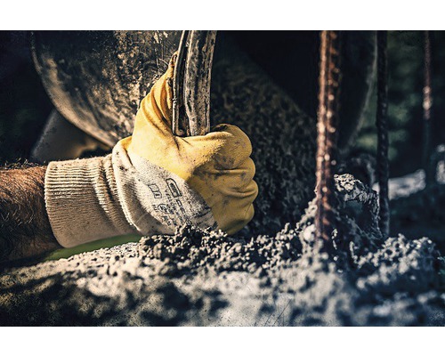 Eine Hand mit Arbeitshandschuh hält ein Werkzeug in der Nähe von Betonstahl.