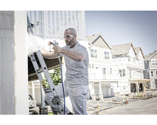 Mann auf einer Leiter, der mit einer Farbspritzpistole ein Haus streicht