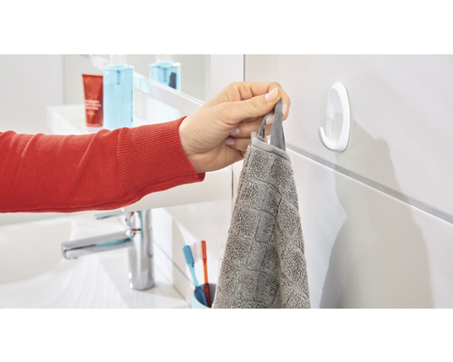 Eine Person hängt ein graues Handtuch an einen weißen Klebehaken im Badezimmer