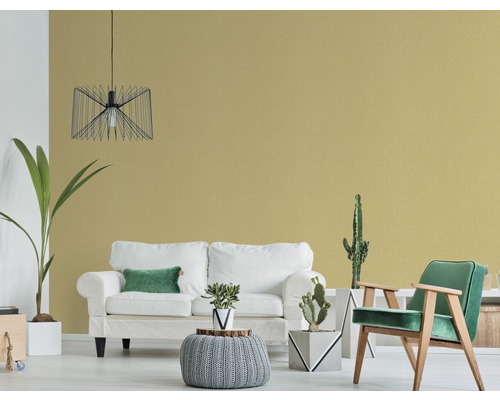 Wohnzimmer mit Sofa, Sessel und Zimmerpflanzen vor einer einfarbigen Wand