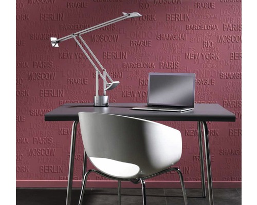 Schreibtisch mit Lampe, Stuhl und Laptop vor einer Wandtapete mit Städtenamen