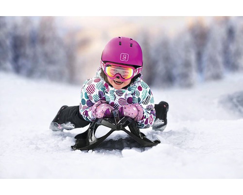 Kind mit Helm und Skibrille auf einem Schlitten im Schnee