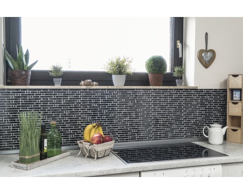 Küchenszene mit Mosaikfliesen, Fensterbank mit Pflanzen, Obstkorb und Kochfeld.