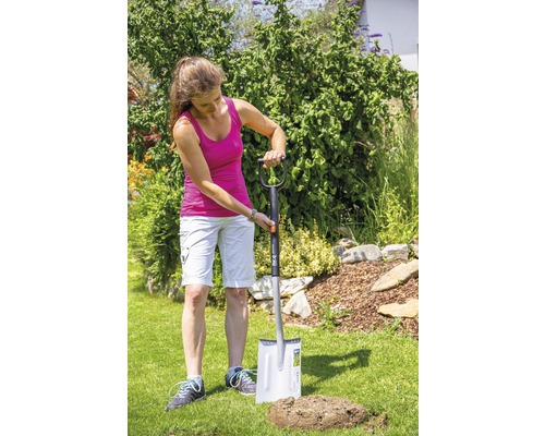 Frau sticht mit einem Spaten ein Loch in den Rasen im Garten.