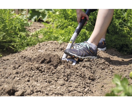 Person arbeitet mit einer Sauzahn-Hacke im Garten.