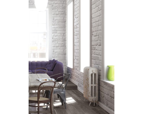 Heller Wohnraum mit Esstisch, Stühlen, Sofa und Heizkörper vor einer Ziegelwand