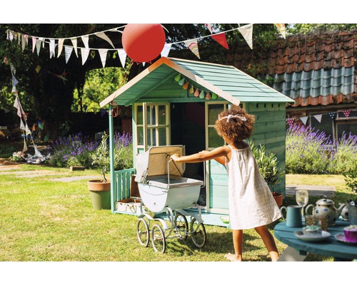 Kind spielt mit Puppenwagen vor Spielhaus im Garten.