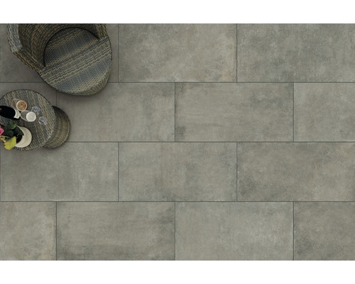 Bodenansicht mit grauen Terrassenfliesen, Rattansessel und kleinem Tisch