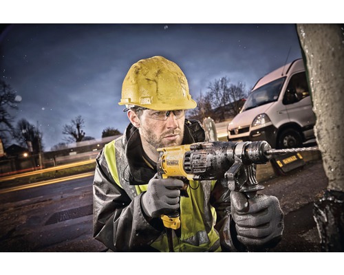Ein Bauarbeiter mit Schutzhelm bohrt mit einer Bohrmaschine in ein Objekt im Freien.