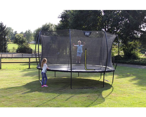 Gartenszene mit einem Trampolin, auf dem ein Kind springt, während ein anderes daneben steht