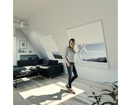 Insektenschutz Windhager Expert Plissee 2in1 für Dachfenster weiss 110x160 cm Wohnraum mit Dachfenstern und Frau, die ein Plissee bedient