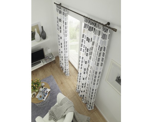 Wohnzimmer mit gemusterten Gardinen, Vorhangstange, Sessel, Teppich und Couchtisch.