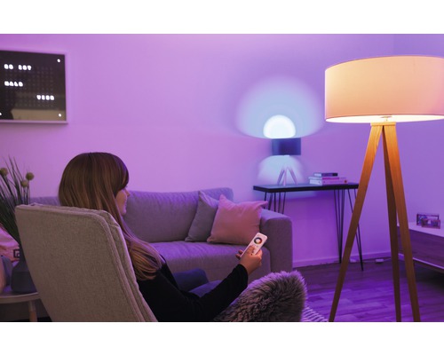 Frau mit Fernbedienung in einem Wohnzimmer mit Stehlampe und Tischlampe.