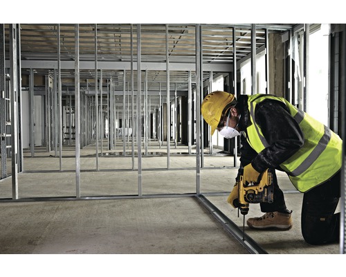 Ein Bauarbeiter befestigt eine Metallschiene mit einem Bohrer in einem Raum mit Metallrahmen.