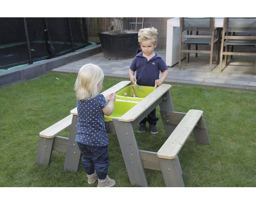 Zwei Kinder spielen an einem grauen Kinderspieltisch mit grünen Wannen im Garten.