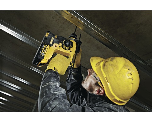 Ein Handwerker befestigt mit einem Akku-Bohrhammer eine Metallschiene an einer Betondecke.