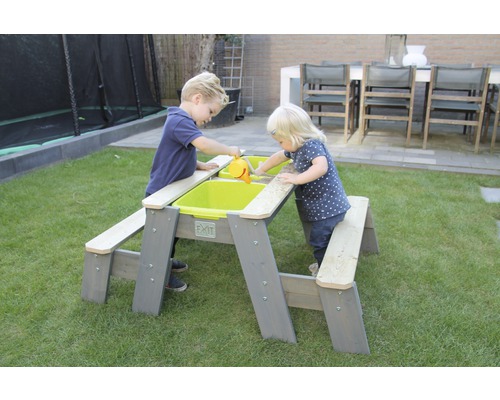 Zwei Kinder spielen an einem EXIT Picknicktisch mit Sand und Wasser im Garten.