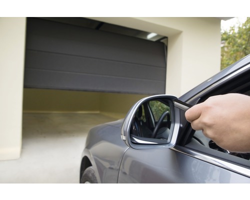 Eine Person öffnet mit einer Fernbedienung ein Garagentor von einem Auto aus.