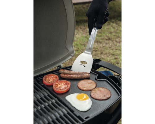 Grill mit Würstchen, Tomaten, Speck und Spiegelei sowie einer Person mit Grillwender