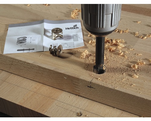 Bohrmaschine bohrt Loch in Holzbrett neben Beschlag und Anleitung