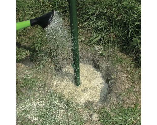 Ein grüner Zaunpfahl wird mit Wasser aus einer Gießkanne befeuchtet.