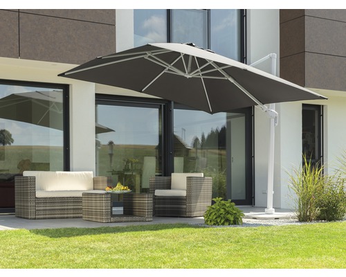 Terrassenszene mit Ampelschirm, Rattansitzgruppe und Couchtisch auf Rasenfläche vor einem Haus