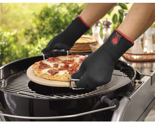 Eine Pizza wird mit Grillhandschuhen auf einen Grill gelegt.