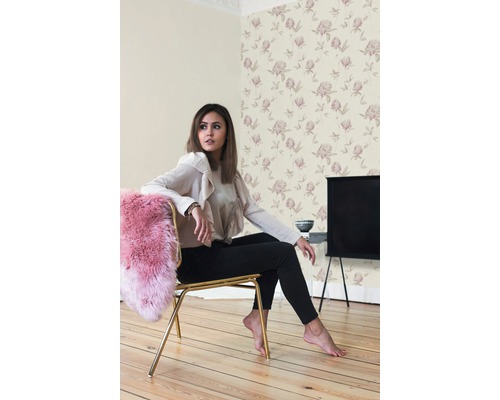 Szene mit einer Frau, die auf einem Stuhl in einem Zimmer mit floraler Tapete sitzt.