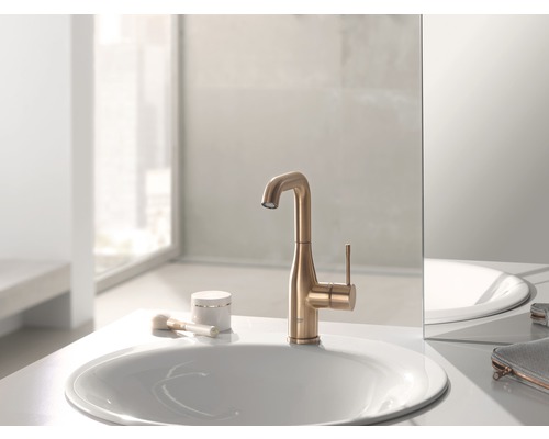 Auf einem Waschtisch steht ein goldfarbener Wasserhahn neben einem Waschbecken.