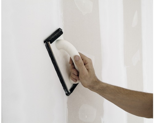 Hand schleift eine Wand mit einem Handschleifer