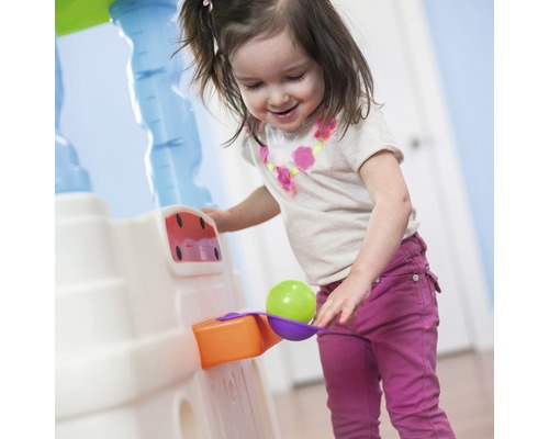Ein lächelndes Mädchen spielt mit einer Spielküche und einem Ball.