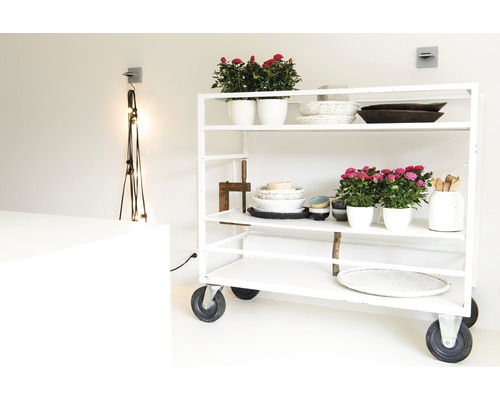 Ein weißes Rollregal mit Blumenschalen, Schüsseln und dekorativen Gegenständen in einem hellen Raum.