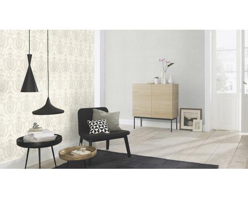 Helles Wohnzimmer mit gemusterter Tapete, Sessel, Kommode und Pendelleuchten.