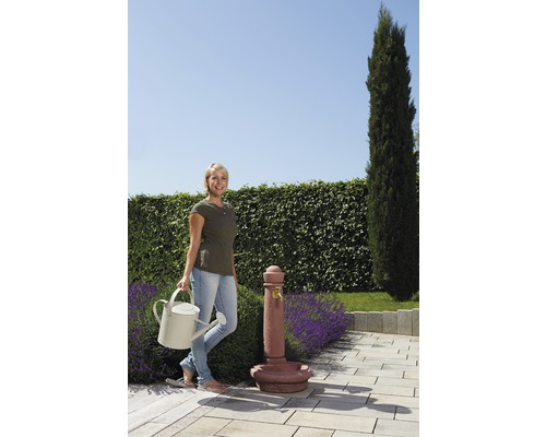 Frau mit Gießkanne neben einem Gartenbrunnen auf einer Terrasse