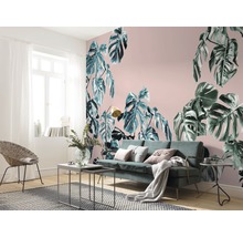Wohnzimmer mit Monstera-Motivtapete, Sofa und Rattansessel.