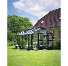 Gewächshaus auf Rasenfläche neben einem Haus mit Ziegeldach.