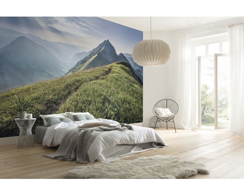 Helles Schlafzimmer mit Berglandschaft-Fototapete, Bett, Sessel, Lampe und hellem Holzboden