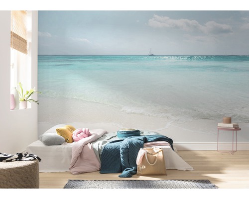 Wohnraum mit Fototapete, die eine Meereslandschaft mit Strand und einem Segelboot zeigt.