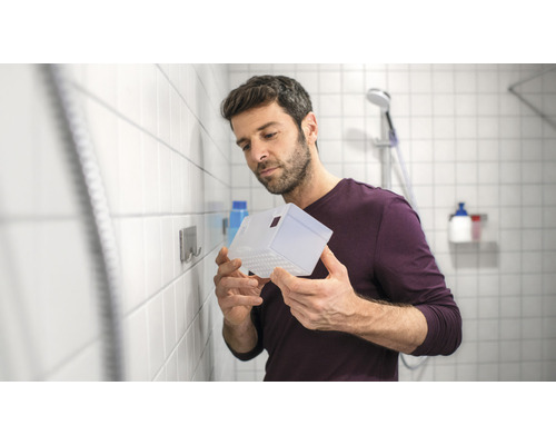 Mann hält eine transparente Duschablage im Badezimmer.